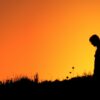 silhouette of woman standing on grass field during sunset